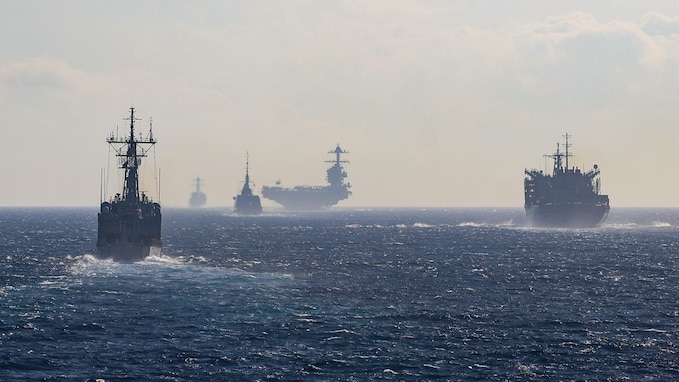 A multinational naval strike group, including U.S. Navy destroyers and an aircraft carrier, sails in formation.