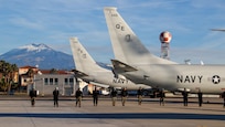 Sailors form a line to conduct a foreign object debris (FOD) walkdown on the flight line at Naval Air Station Sigonella, Sicily, ensuring the area is safe for aircraft operations.