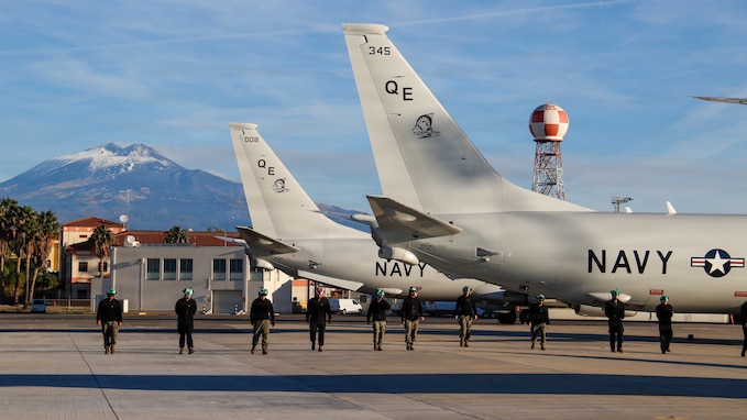 Sailors form a line to conduct a foreign object debris (FOD) walkdown on the flight line at Naval Air Station Sigonella, Sicily, ensuring the area is safe for aircraft operations.