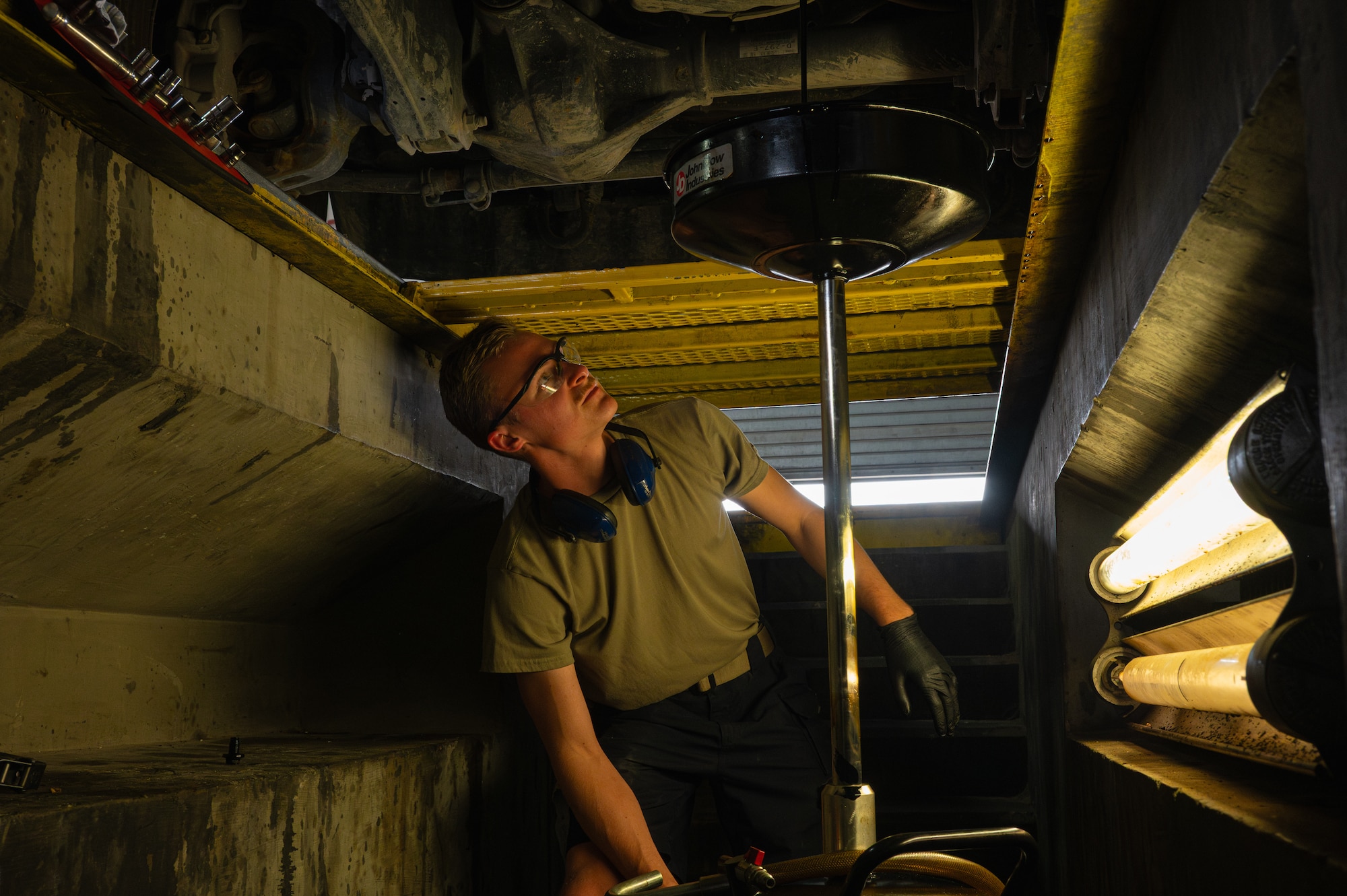 An Airman watches as oil from a truck pours out into an oil pan