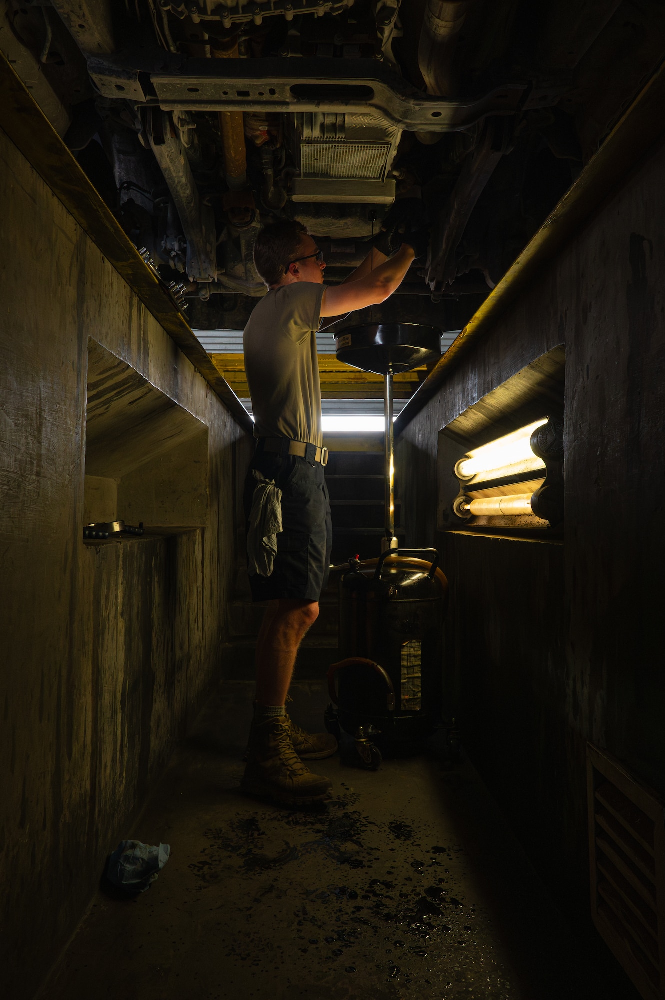 An Airman stands in an area underground changing the oil of a truck