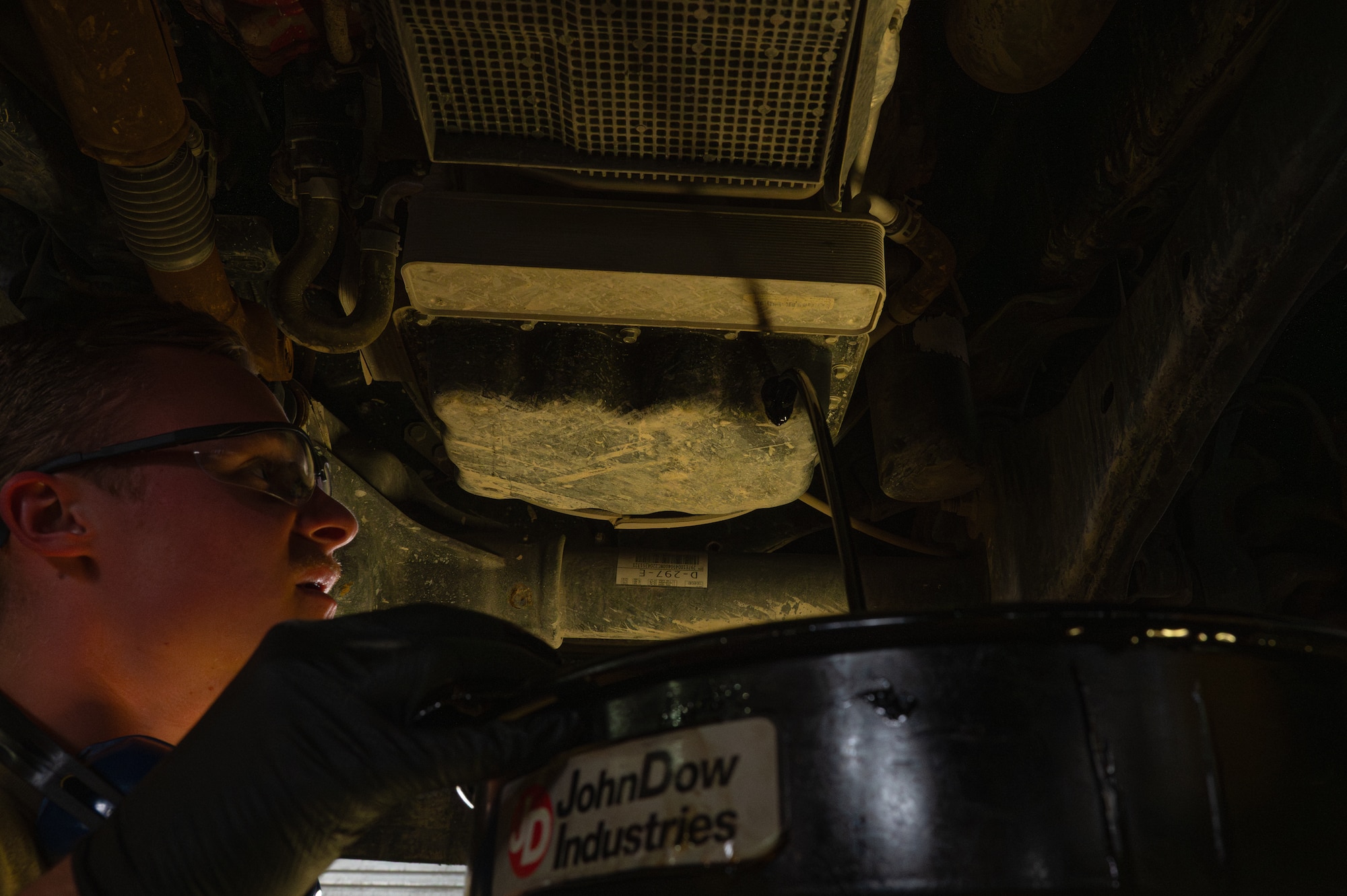 An Airman holds an oil pan under a vehicle