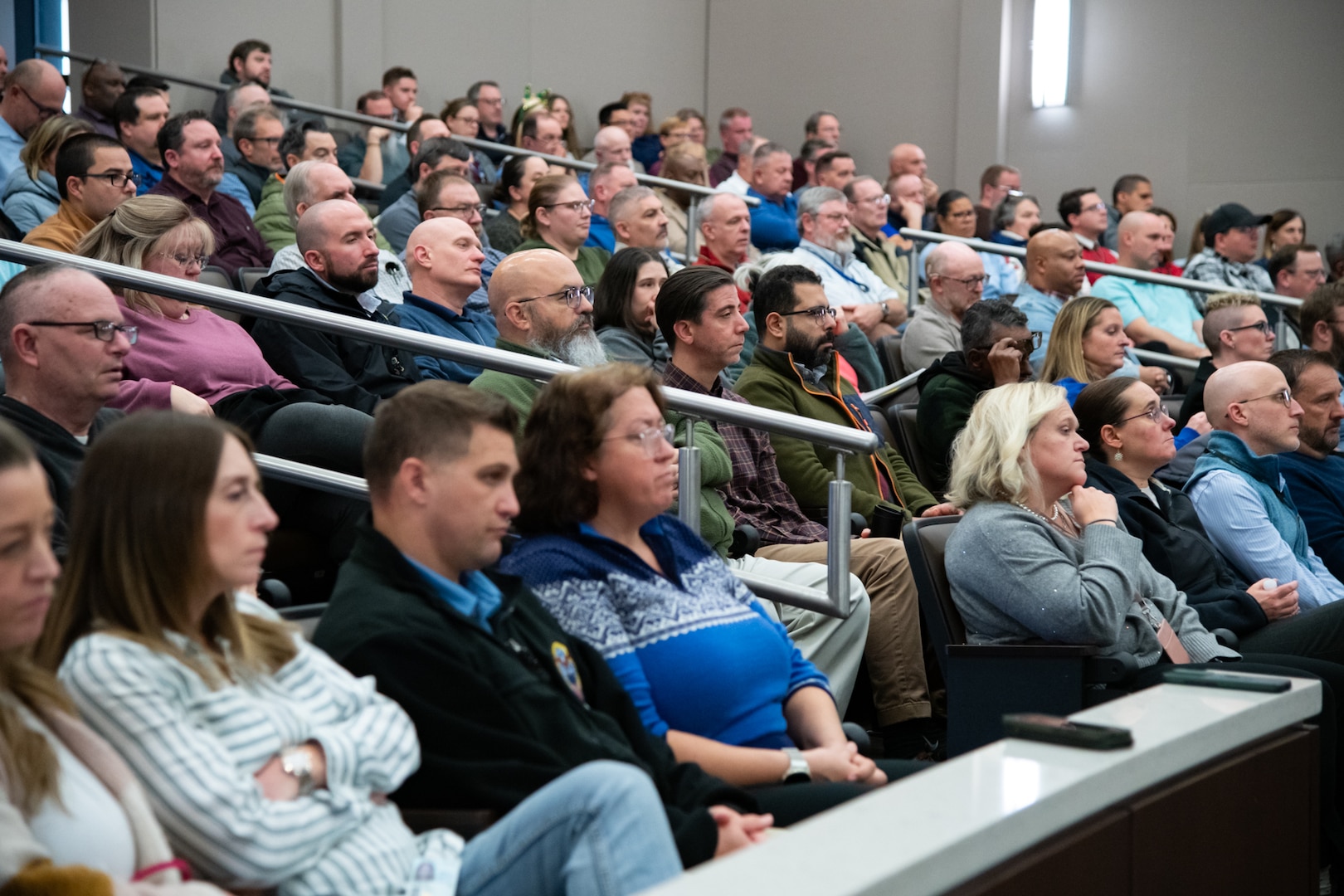 A large crowd of people are seated in an indoor auditorium looking forward.