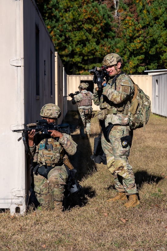 One person kneels while holding a rifle and another person stands while holding a rifle