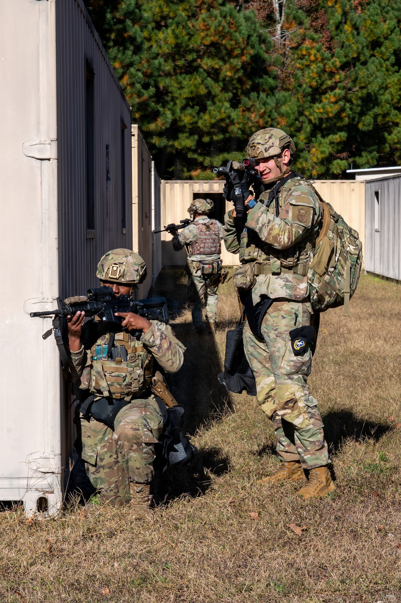 One person kneels while holding a rifle and another person stands while holding a rifle