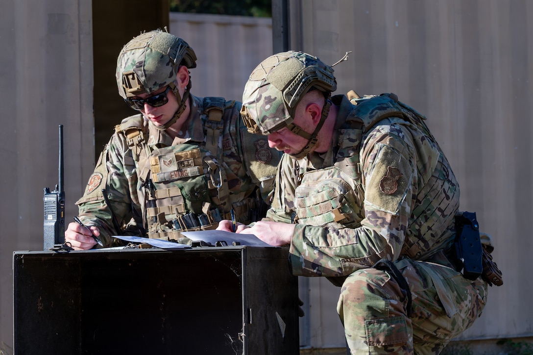 Two men kneel over and write on a piece of paper.