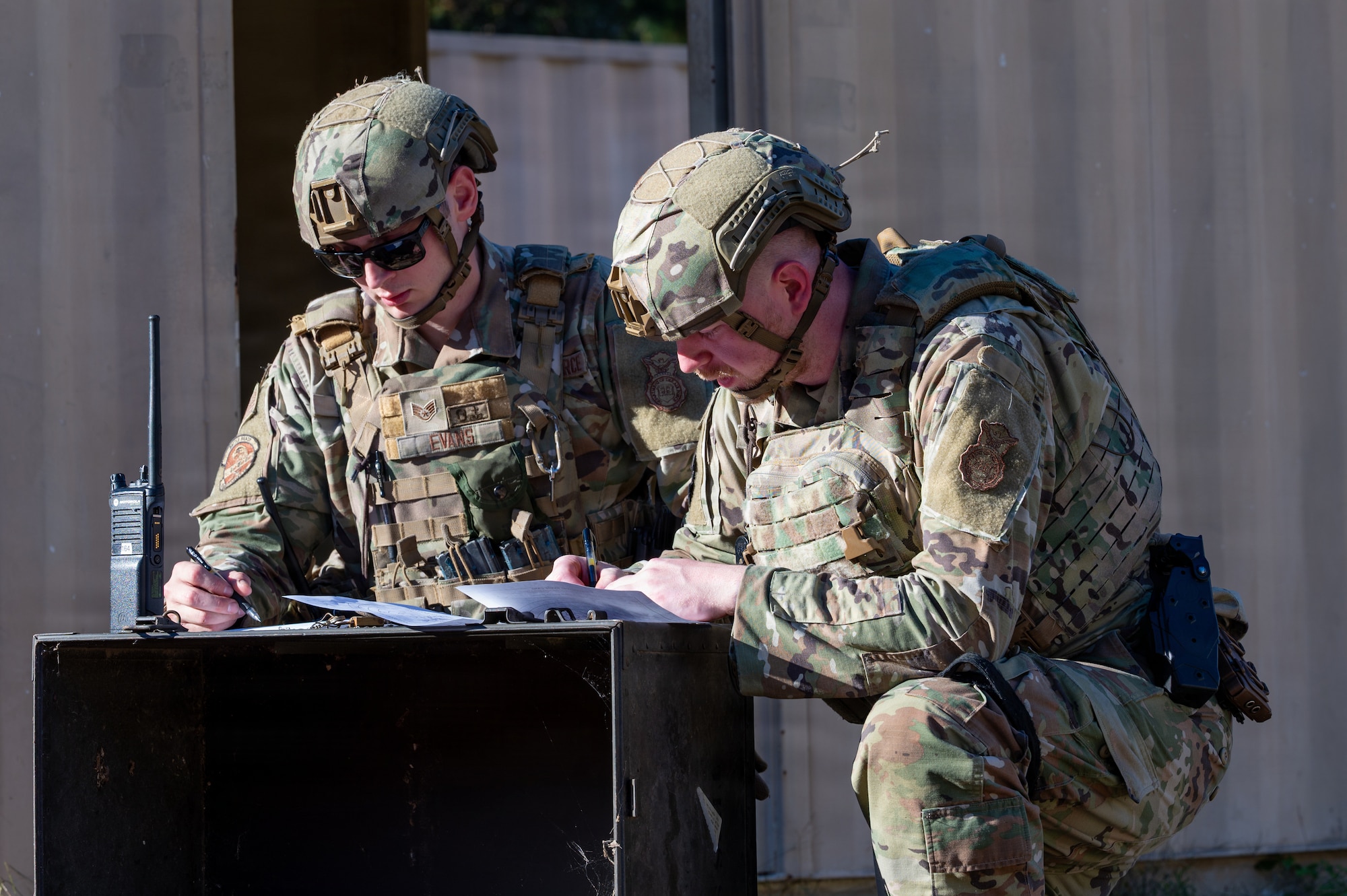 Two men kneel over and write on a piece of paper.