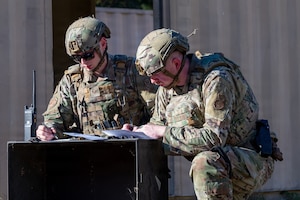Two men kneel over and write on a piece of paper.