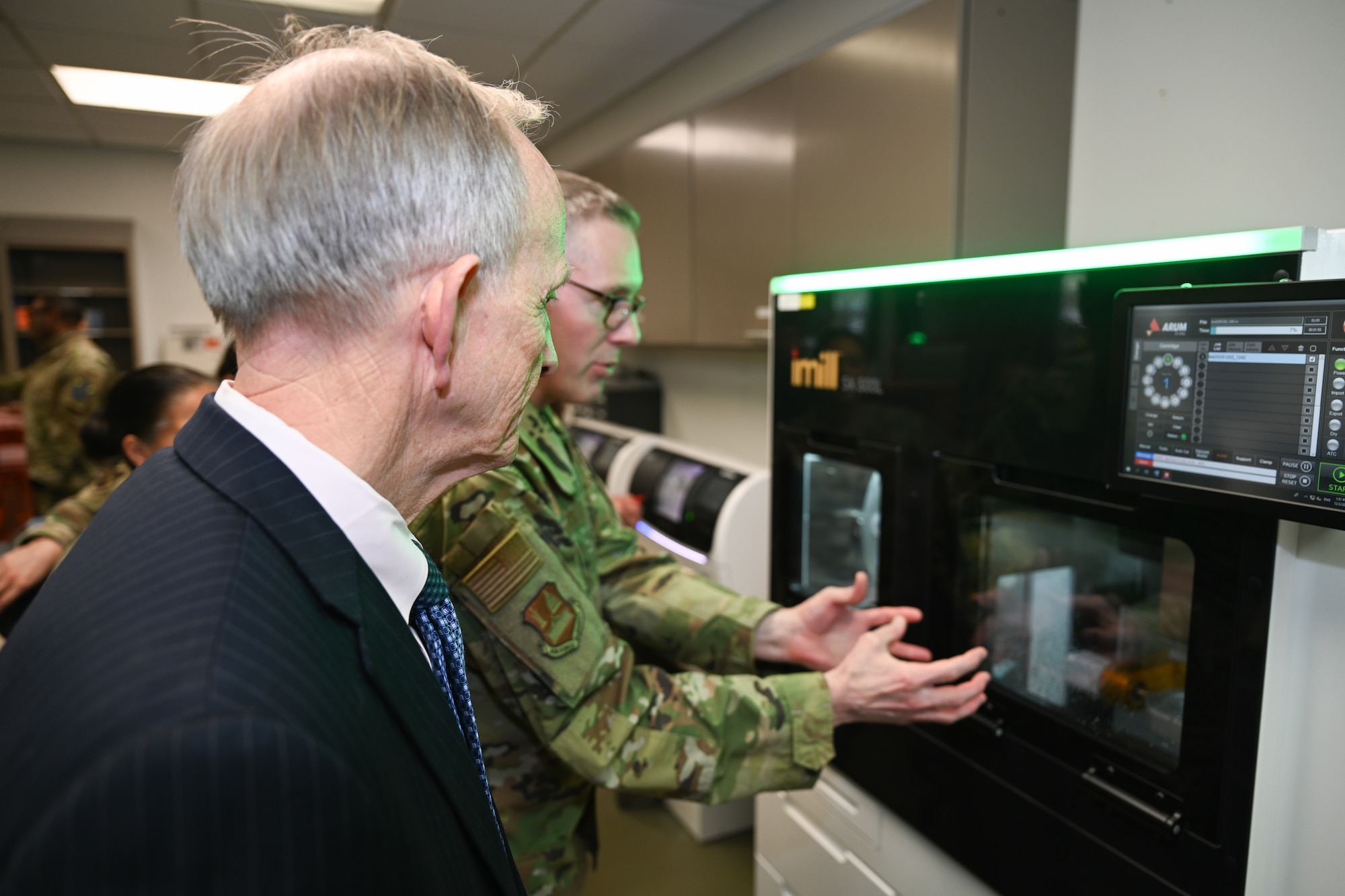 Dr. Smith stands in front of a fabrication machine as Col. Sheets stands next to him describing how the machine works.