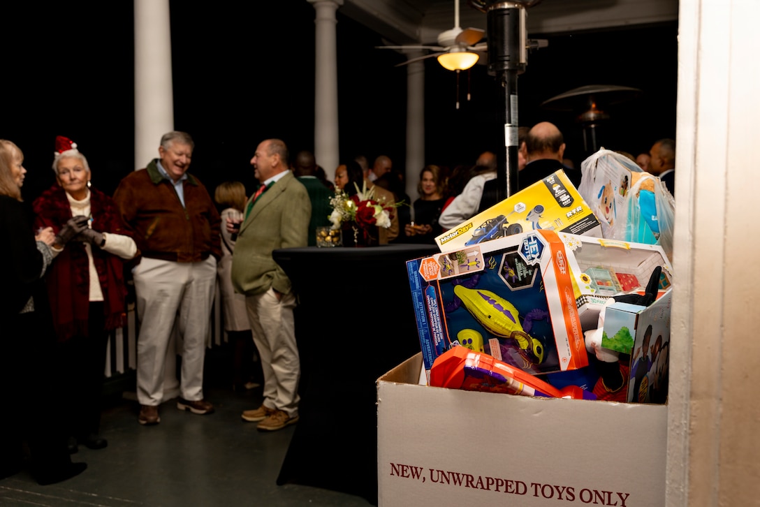Toys sit in a Toys for Tots collection box as guests mingle in the background during the Christmas party hosted by the Commander of Marine Forces Reserve and Marine Forces South at Quarters A in New Orleans, Dec. 6, 2025. The event supported the Marine Corps Reserve Toys for Tots program, with attendees contributing donations throughout the evening. (U.S. Marine Corps photo by Sgt. Samuel Qin)
