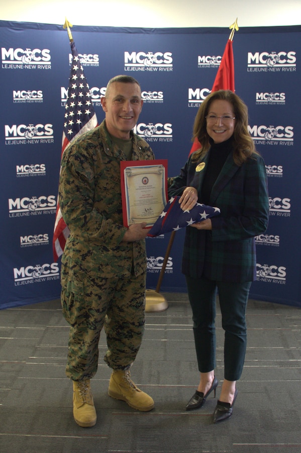 U.S. Marine Corps Brig. Gen. Ralph J. Rizzo, Jr., commanding general, Marine Corps Installations East – Marine Corps Base (MCIEAST-MCB) Camp Lejeune presents a folded National Ensign to Sarah Wiltgen at her retirement ceremony at MCCS headquarters on MCB Camp Lejeune, Dec. 12, 2025. During her 11-year tenure as assistant chief of staff for Marine Corps Community Services, MCIEAST, Wiltgen's steadfast leadership was pivotal in navigating MCCS’s support of MCIEAST installations through major challenges to include Hurricane Florence and the COVID-19 pandemic. She was a dedicated advocate for Marines, sailors, and their families, championing several highly-successful pilot programs that directly enhanced their well-being.