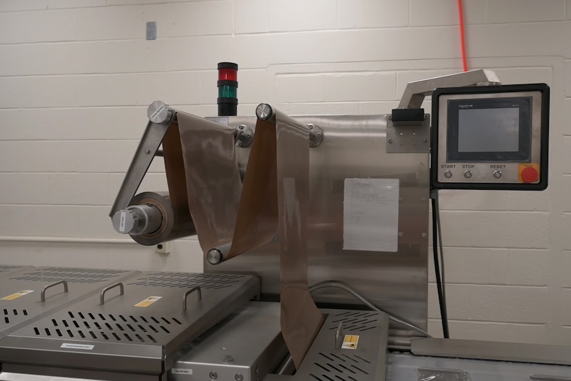 An industrial machine has a monitor with buttons and plastic sheets being fed into it.
