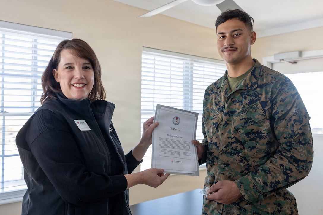 Lauren Bolen, interim director of the American Red Cross, left, presents Cpl. Malikah Warren, 2nd Distribution Support Battalion, 2nd Marine Logistics Group, right, with the Red Cross Lifesaving Award on Marine Corps Base Camp Lejeune, North Carolina, Dec. 16, 2025. The Marines received the Lifesaving Award, the second highest award the American Red Cross bestows, for rescuing people during an emergency at a local beach earlier this year. (U.S. Marine Corps photo by Lance Cpl. Erica S. Padgett)