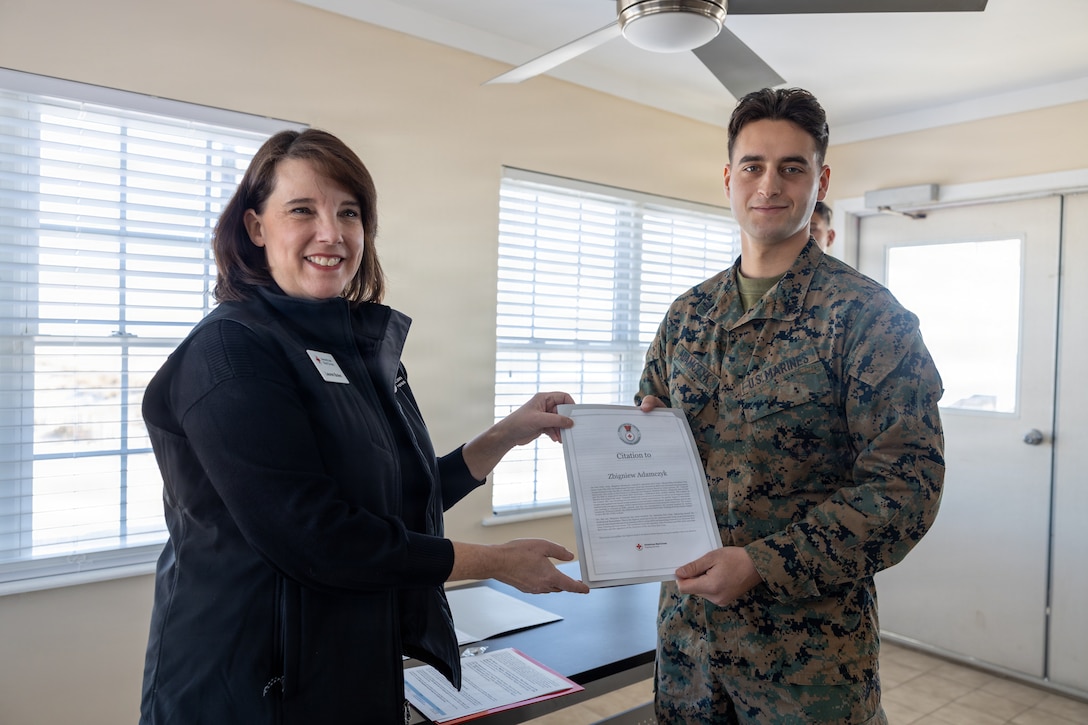 Lauren Bolen, interim director of the American Red Cross, presents Cpl. Zbigniew Adamczyk, Marine Medium Tiltrotor Training Squadron 204, Marine Aircraft Group 26, 2nd Marine Aircraft Wing, with the Red Cross Lifesaving Award on Marine Corps Base Camp Lejeune, North Carolina, Dec. 16, 2025. The Marines received the Lifesaving Award, the second highest award the American Red Cross bestows, for rescuing people during an emergency at a local beach earlier this year. (U.S. Marine Corps photo by Lance Cpl. Erica S. Padgett)
