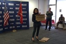 Sarah Wiltgen, assistant chief of staff, Marine Corps Community Services, Marine Corps Installations East, poses with a gift presented to her by the staff on the occasion of her retirement at MCCS headquarters on Marine Corps Base Camp Lejeune, Dec. 12, 2025.