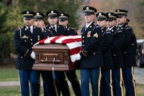 Army Soldiers in ceremonial dress uniforms are carrying a US flag-draped casket during a funeral