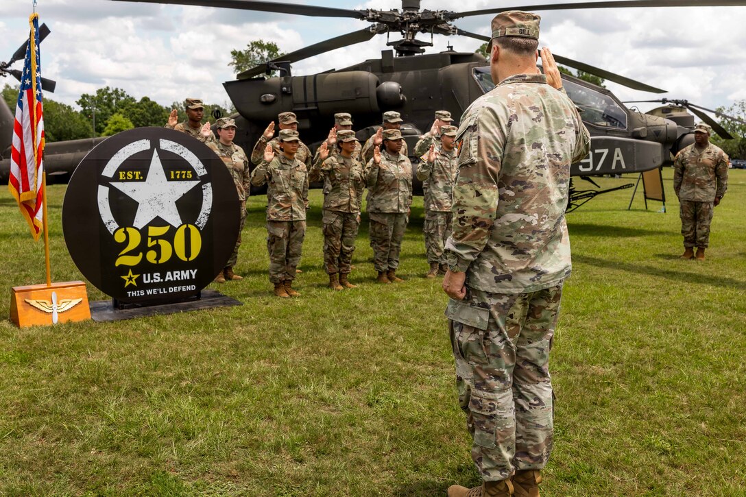 A general holds up an arm as soldiers standing in front of a helicopter mimic the salute.