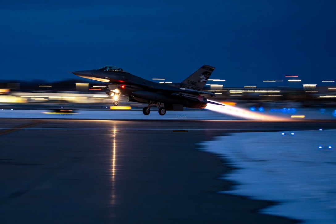 An aircraft takes off from a blurred snowy tarmac in the dark illuminated by white lights.
