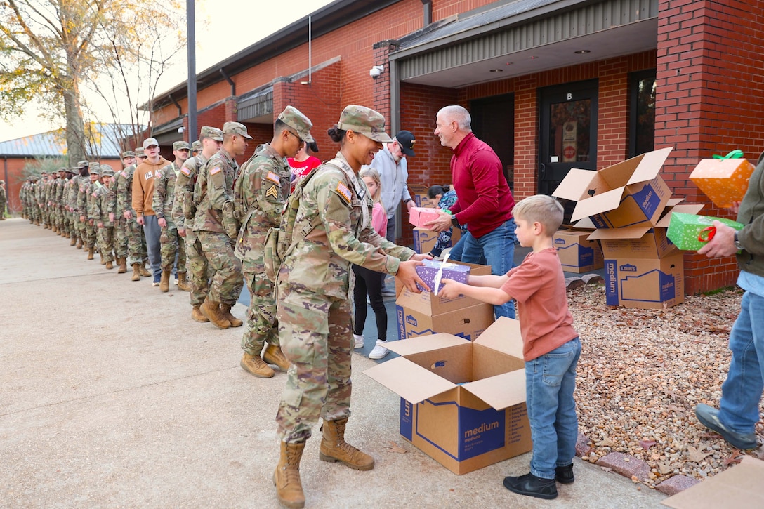Volunteers hand boxes to soldiers standing in line in front of a building during the day.