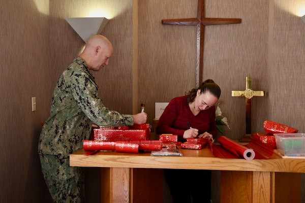 TWENTYNINE PALMS, Calif. (Dec. 17, 2025) — Navy Chaplain Lt. Cmdr. Nicholas Suddath (left) and Command Ombudsman Jennifer Belding (right) wrap holiday gifts during the Angel Tree program at Naval Hospital Twentynine Palms. The community-driven initiative anonymously connects volunteers with military children in need, helping make the holiday season brighter for Sailors and their families. (U.S. Navy photo by Christopher Jones/NMRTC Twentynine Palms Public Affairs Officer)