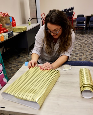 TWENTYNINE PALMS, Calif. (Dec. 17, 2025) — Contract Patient Safety Specialist Alisha Moreno wraps holiday gifts as a volunteer during the Angel Tree program at Naval Hospital Twentynine Palms. The community-driven initiative anonymously connects volunteers with military children in need, helping support Sailors’ families throughout the holiday season. (U.S. Navy photo by Christopher Jones/NMRTC Twentynine Palms Public Affairs Officer)