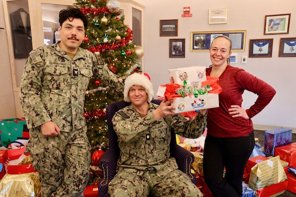 TWENTYNINE PALMS, Calif. (Dec. 17, 2025) — Navy Chaplain Lt. Cmdr. Nicholas Suddath (center), Religious Program Specialist 3rd Class Diego Escalante (left) and Command Ombudsman Jennifer Belding (right) pose in front of donated gifts during the Angel Tree program at Naval Hospital Twentynine Palms. The community-driven initiative provided more than 250 holiday gifts to 83 military children this year, anonymously connecting volunteers with Sailors’ families in need and helping make the holiday season brighter across the command. (U.S. Navy photo by Christopher Jones/NMRTC Twentynine Palms Public Affairs Officer)