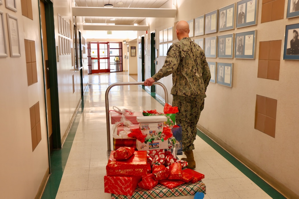TWENTYNINE PALMS, Calif. (Dec. 17, 2025) — Lt. Cmdr. Nicholas Suddath, chaplain at Naval Hospital Twentynine Palms, wheels a cart of donated toys to place beneath the hospital’s Angel Tree as part of the annual holiday program. The community-driven initiative anonymously connects volunteers with military children in need, providing holiday gifts to help support Sailors and their families during the season. (U.S. Navy photo by Christopher Jones/NMRTC Twentynine Palms Public Affairs Officer)