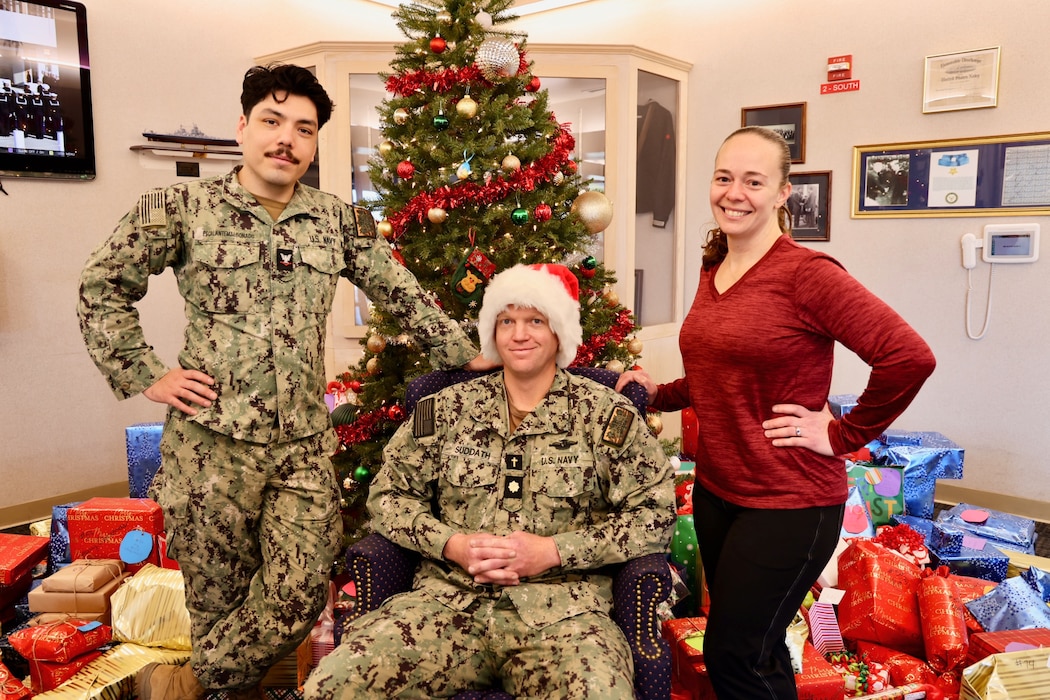 TWENTYNINE PALMS, Calif. (Dec. 17, 2025) — Navy Chaplain Lt. Cmdr. Nicholas Suddath (center), Religious Program Specialist 3rd Class Diego Escalante (left) and Command Ombudsman Jennifer Belding (right) pose in front of donated gifts during the Angel Tree program at Naval Hospital Twentynine Palms. The community-driven initiative provided more than 250 holiday gifts to 83 military children this year, anonymously connecting volunteers with Sailors’ families in need and helping make the holiday season brighter across the command. (U.S. Navy photo by Christopher Jones/NMRTC Twentynine Palms Public Affairs Officer)