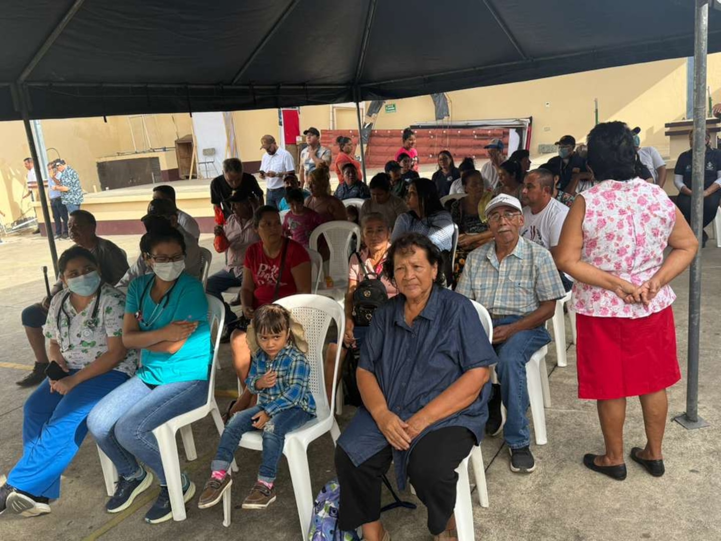 Civilians sit in chairs underneath a tent.