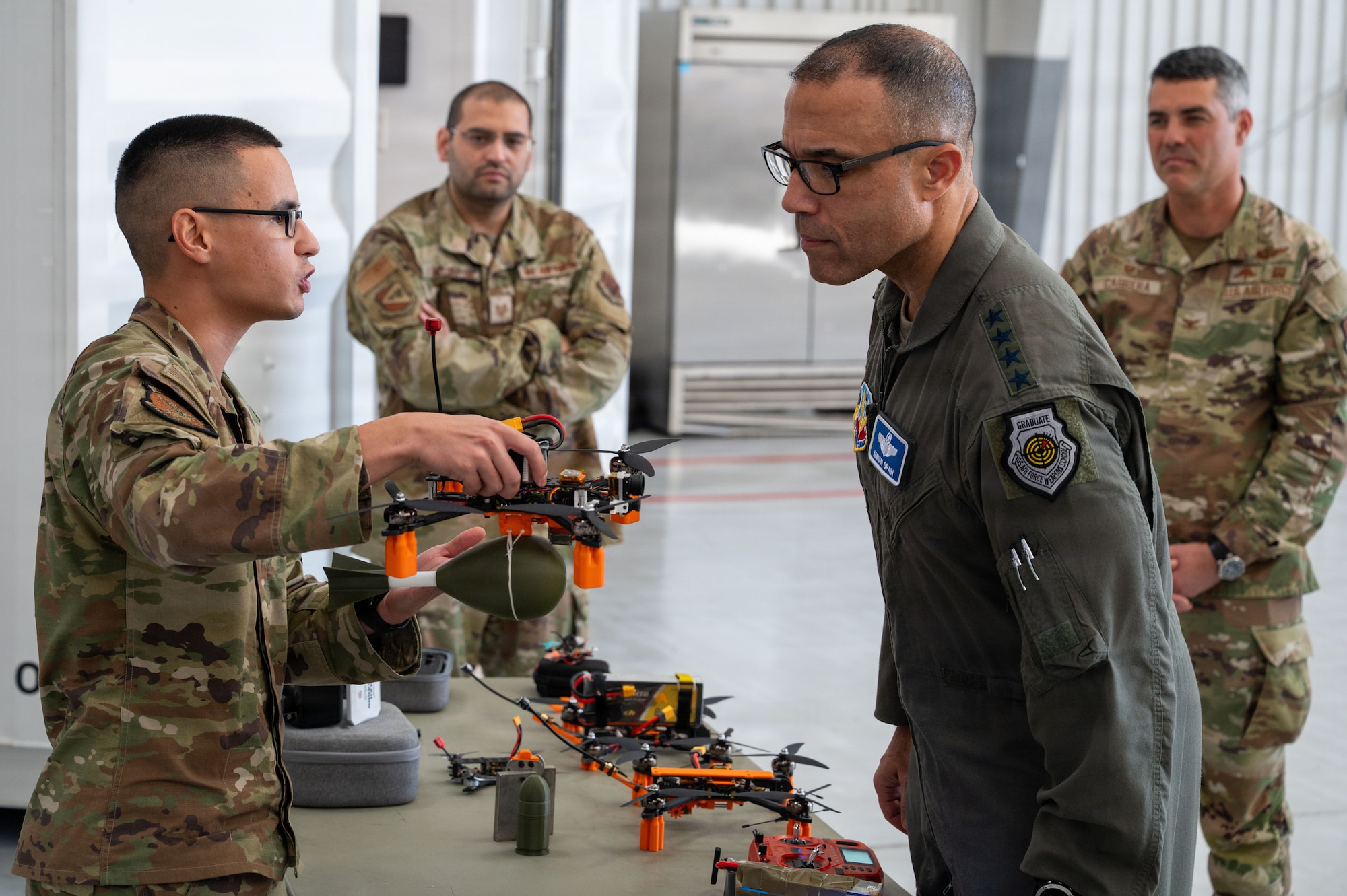 U.S. Air Force Tech Sgt. Joseph Peterson, 48th Rescue Squadron drone innovator, showcases newly implemented unmanned aircraft system capabilities to Gen. Adrian Spain, commander of Air Combat Command, at Davis-Monthan Air Force Base, Arizona, Dec. 16, 2025. Spain was shown the new UAS program where Airmen produced 10 mission-ready drones for $10,000 total, compared to the roughly $40,000 per aircraft often required for commercial systems. (U.S. Air Force photo by Senior Airman Jasmyne Bridgers-Matos)