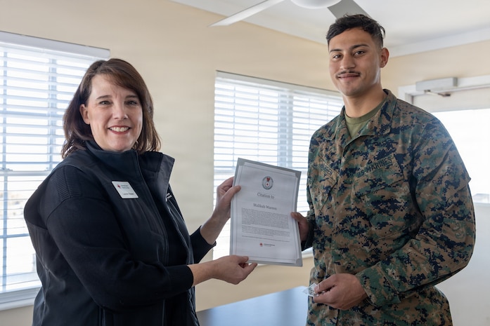 Lauren Bolen, interim director of the American Red Cross, left, presents Cpl. Malikah Warren, 2nd Distribution Support Battalion, 2nd Marine Logistics Group, right, with the Red Cross Lifesaving Award on Marine Corps Base Camp Lejeune, North Carolina, Dec. 16, 2025. The Marines received the Lifesaving Award, the second highest award the American Red Cross bestows, for rescuing people during an emergency at a local beach earlier this year. (U.S. Marine Corps photo by Lance Cpl. Erica S. Padgett)