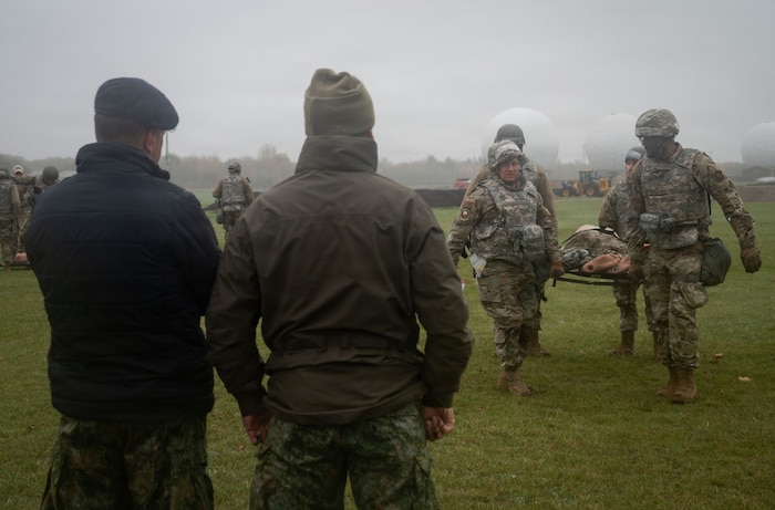 Military members carry a mannequin on a stretcher.