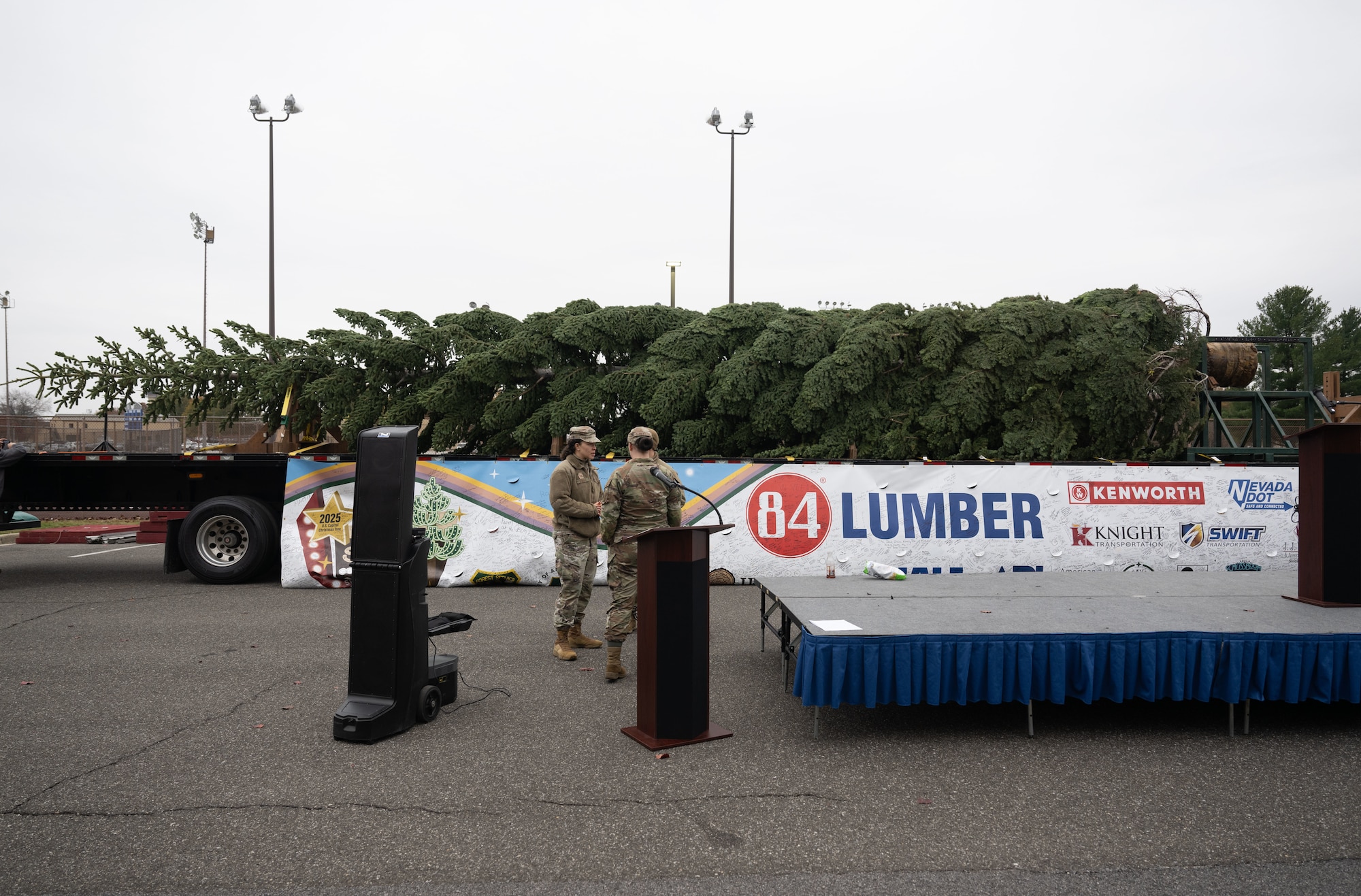 Two people standing next to a 53 foot Christmas tree laying on its side on a truck bed.