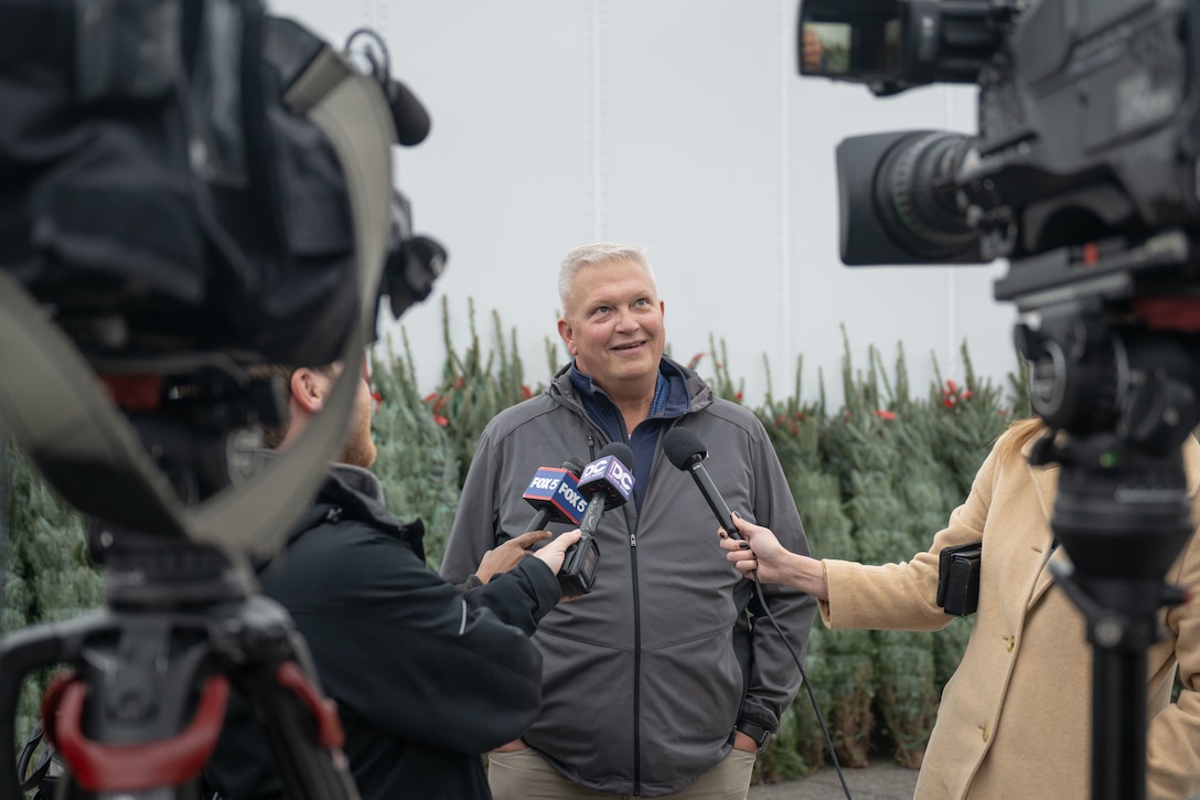 Man speaks into microphone for a news team holding cameras pointed on him.