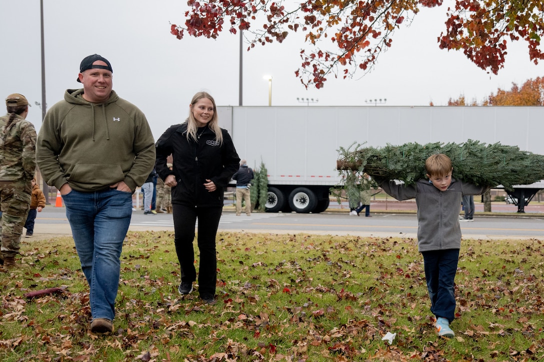 Father and mother walk next to son who is carrying a Christmas tree.