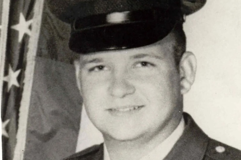 A man in a cap and military dress uniform smiles for a photo.
