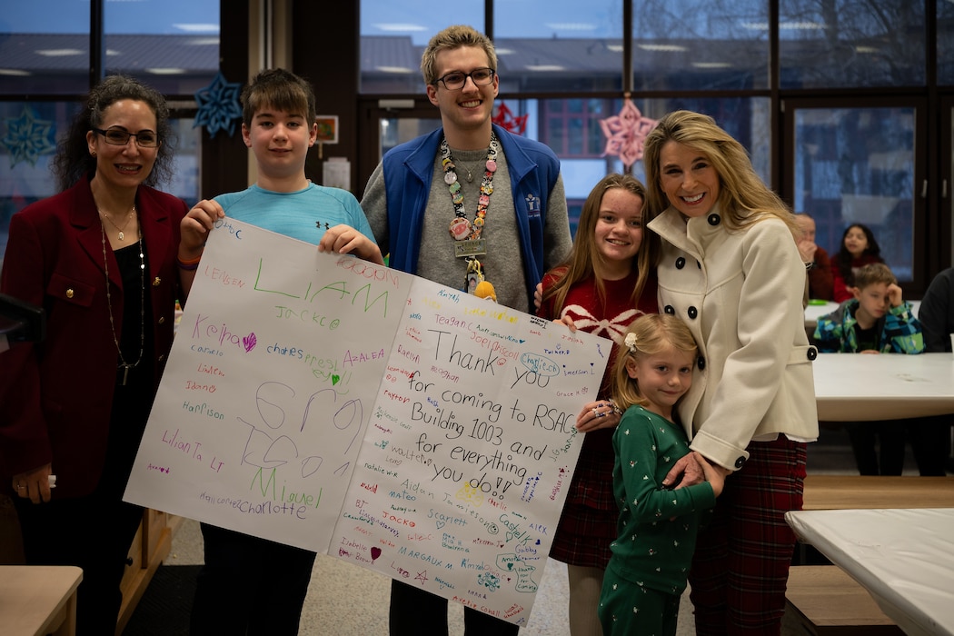 Mrs. Cindy Wilsbach, right, wife of Air Force Chief of Staff Gen. Ken Wilsbach and Dr. Doniel Wolfe, left, wife of Chief Master Sgt. of the Air Force David Wolfe, pose for a group photo with students and faculty of the Ramstein School Age Center at Ramstein Air Base, Germany, Dec. 23, 2025. The visit showcased the 86th Airlift Wing’s focus on creating community by bringing leaders and families together in meaningful ways. (U.S. Air Force photo by Senior Airman Edgar Grimaldo)