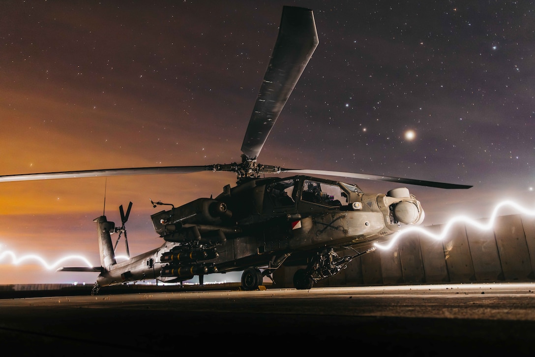A white streak goes across a helicopter as it sits on a ship under a starry, orange night sky.