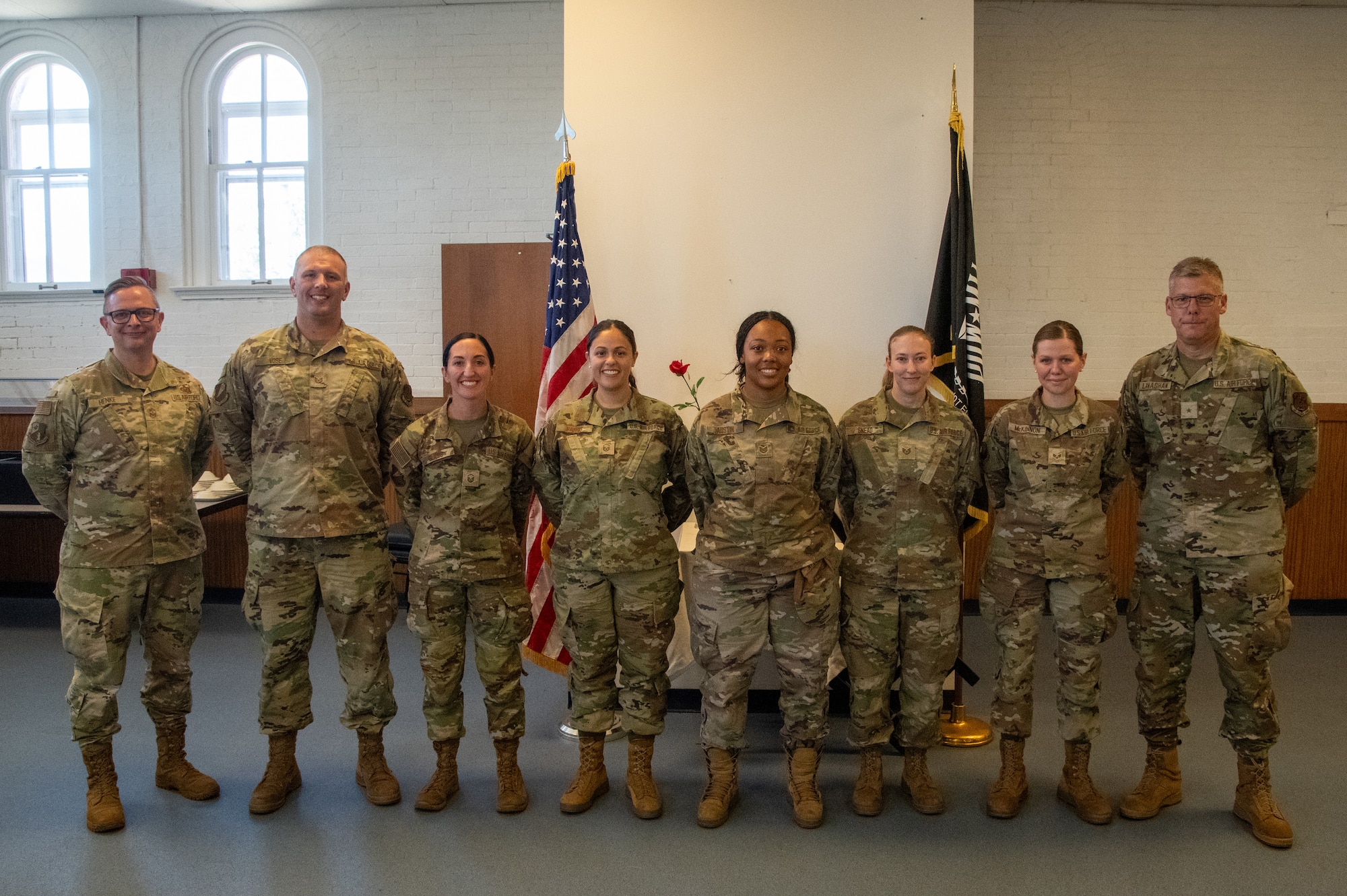 Eight Air National Guard Airmen pose for a group photo in front of a flag display. They are wearing OCP Pattern uniforms.