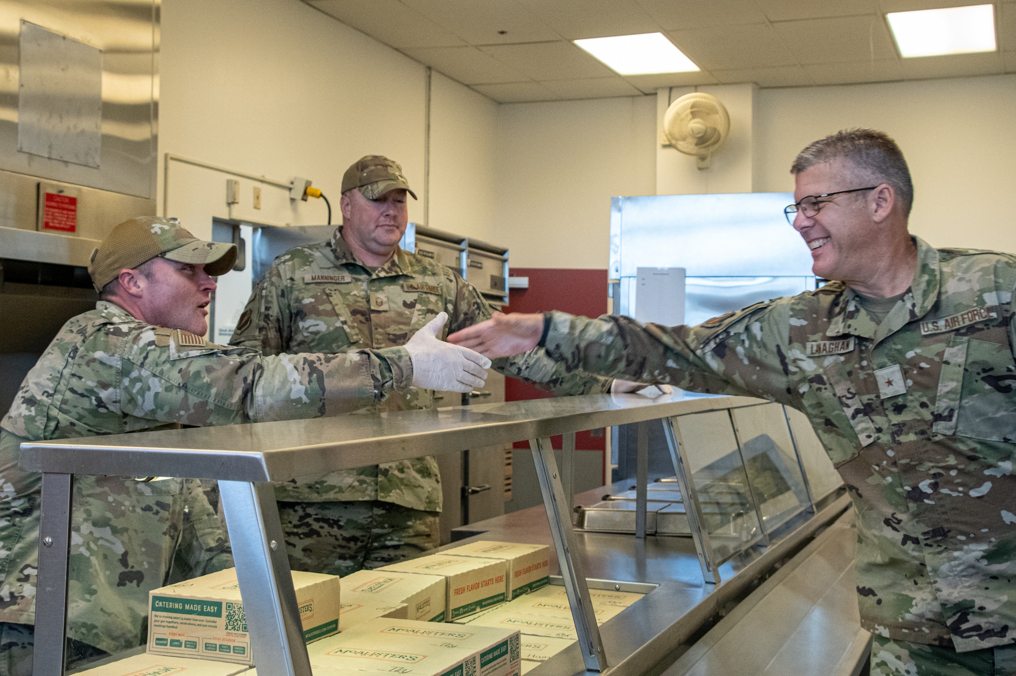 Three Air National Guard Airmen shake hands in a dining facility. They are wearing OCP pattern uniforms.