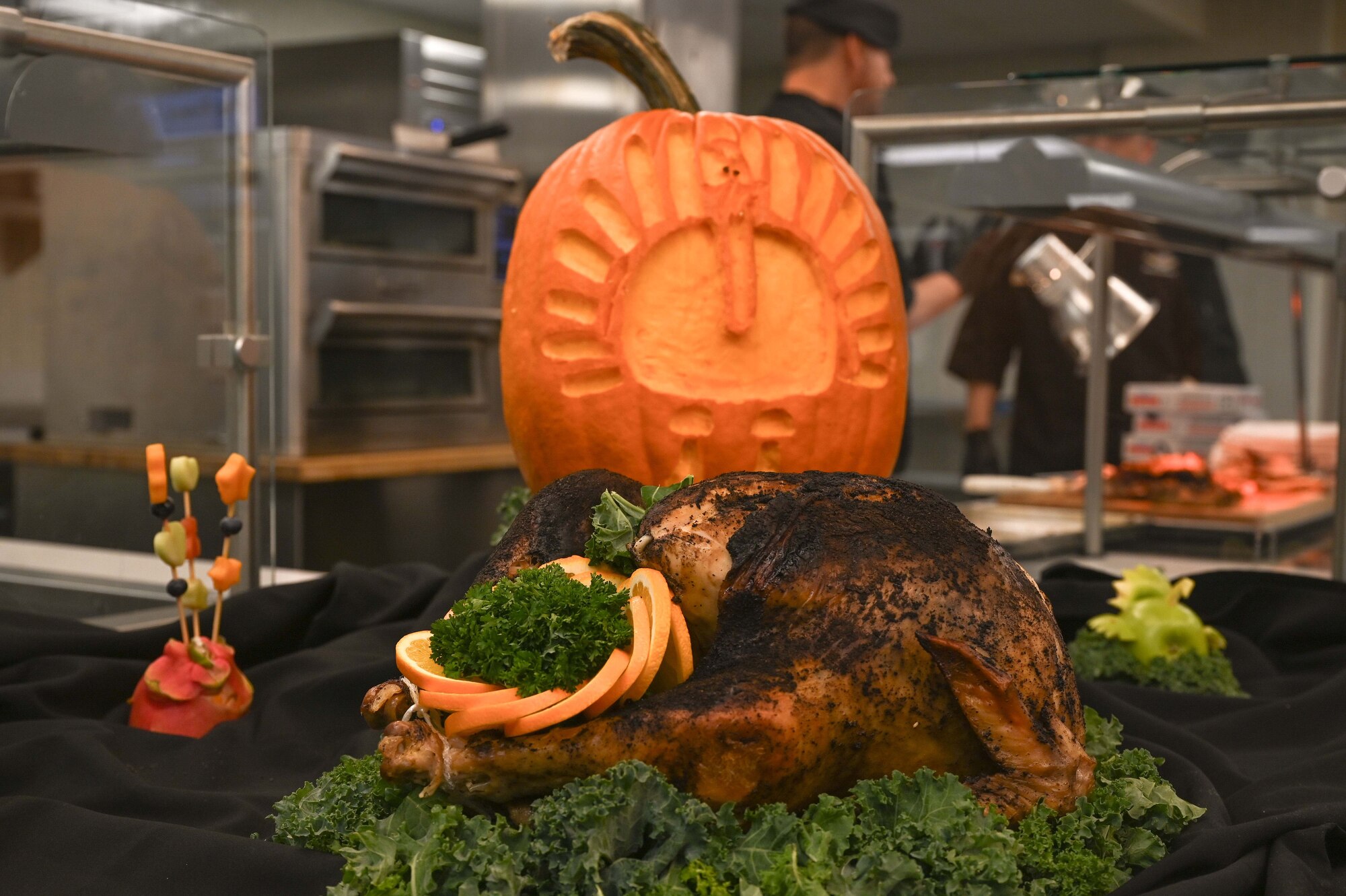 A turkey carved pumpkin rests behind a garnished whole smoked turkey in the Desert Inn Dining Facility at Davis-Monthan Air Force Base, Arizona, Nov. 27, 2025. Throughout the holiday season, the 355th Wing took time to remember the Airmen at home and in deployed locations who make sacrifices to protect the Nation. (U.S. Air Force photo by Staff Sgt. Kahdija Slaughter)