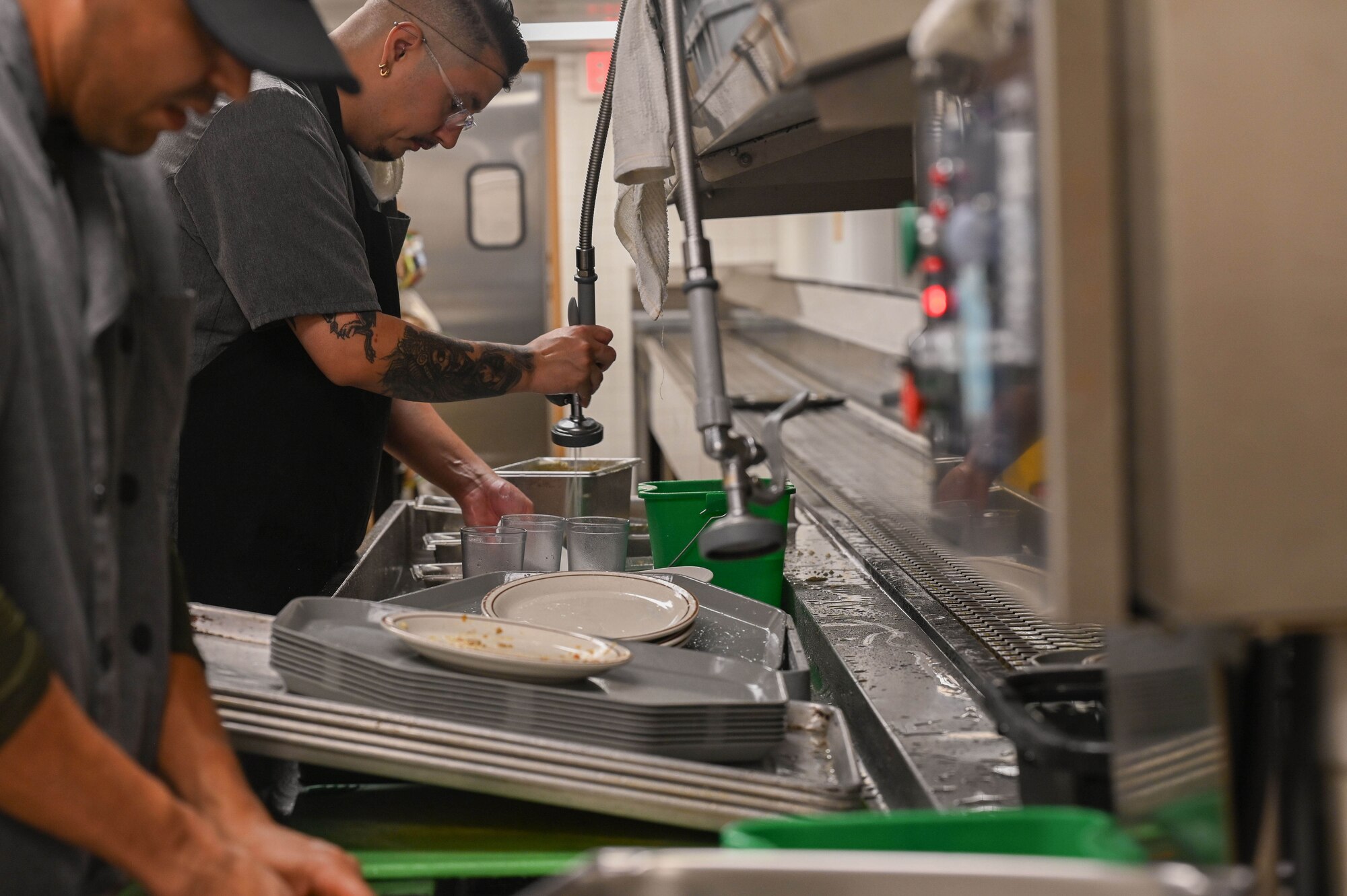 Mess attendants contracted by the 355th Force Support Squadron Dining Facility rinse dishes before loading the dishwasher during the Thanksgiving Day meal at Davis-Monthan Air Force Base, Arizona, Nov. 27, 2025. This year, the DFAC prepared a traditional thanksgiving meal for over 200 servicemembers, veterans, and their families. (U.S. Air Force photo by Staff Sgt. Kahdija Slaughter)