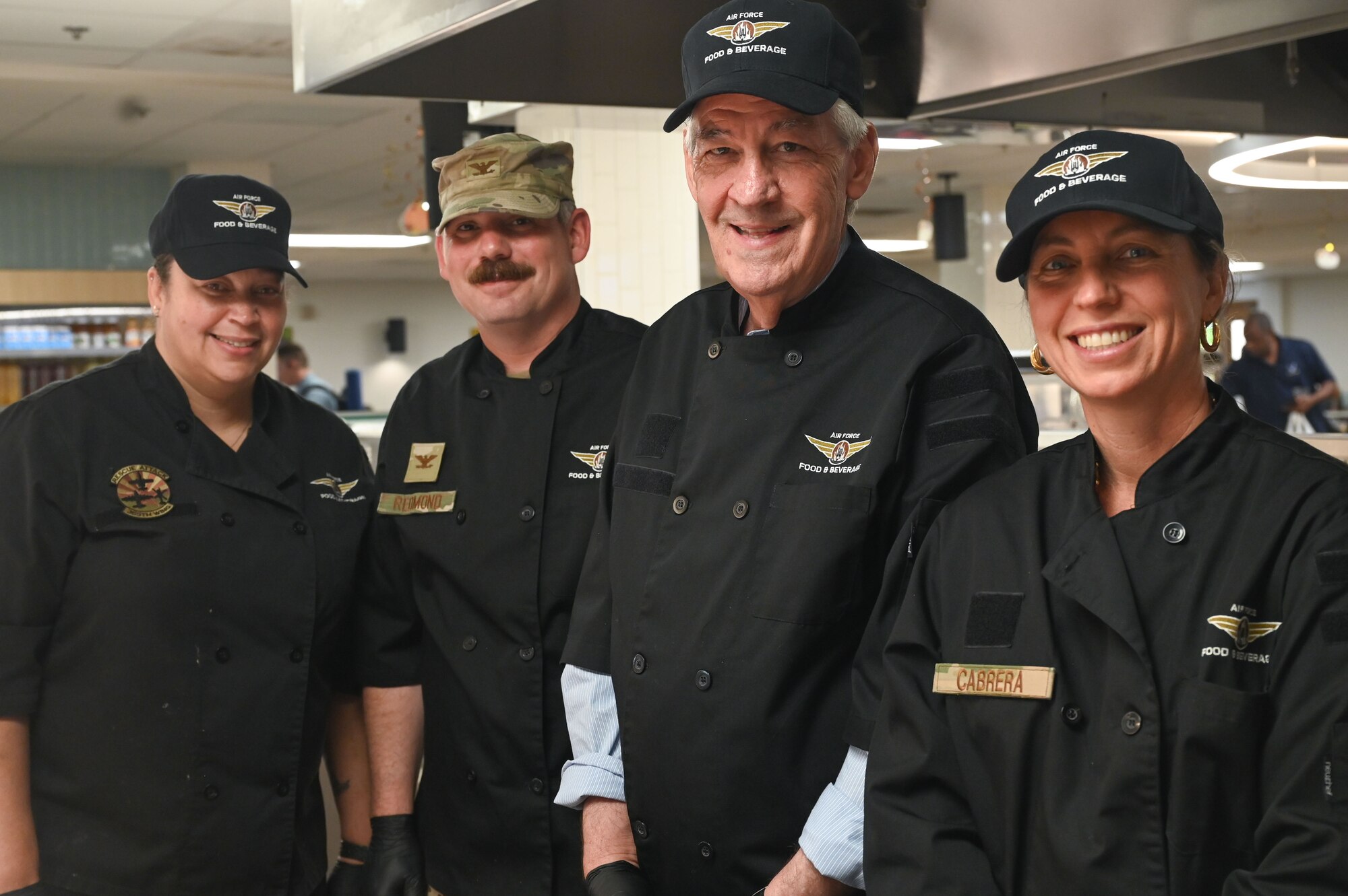 U.S. Air Force Col. Charles Redmond, 355th Wing Deputy Commander, center left, and Mark Irvin, local civic leader, center right, pose for a photo with spouses of 355th Wing senior leaders on Thanksgiving day at Davis-Monthan Air Force Base, Arizona, Nov. 27, 2025. More than 15 of DM’s senior leaders and their spouses donned Desert Inn Dining Facility apparel to serve a fresh cooked holiday meal – a long-standing military tradition for U.S. dining facilities across the Air Force on Thanksgiving Day and Christmas Day. (U.S. Air Force photo by Staff Sgt. Kahdija Slaughter)