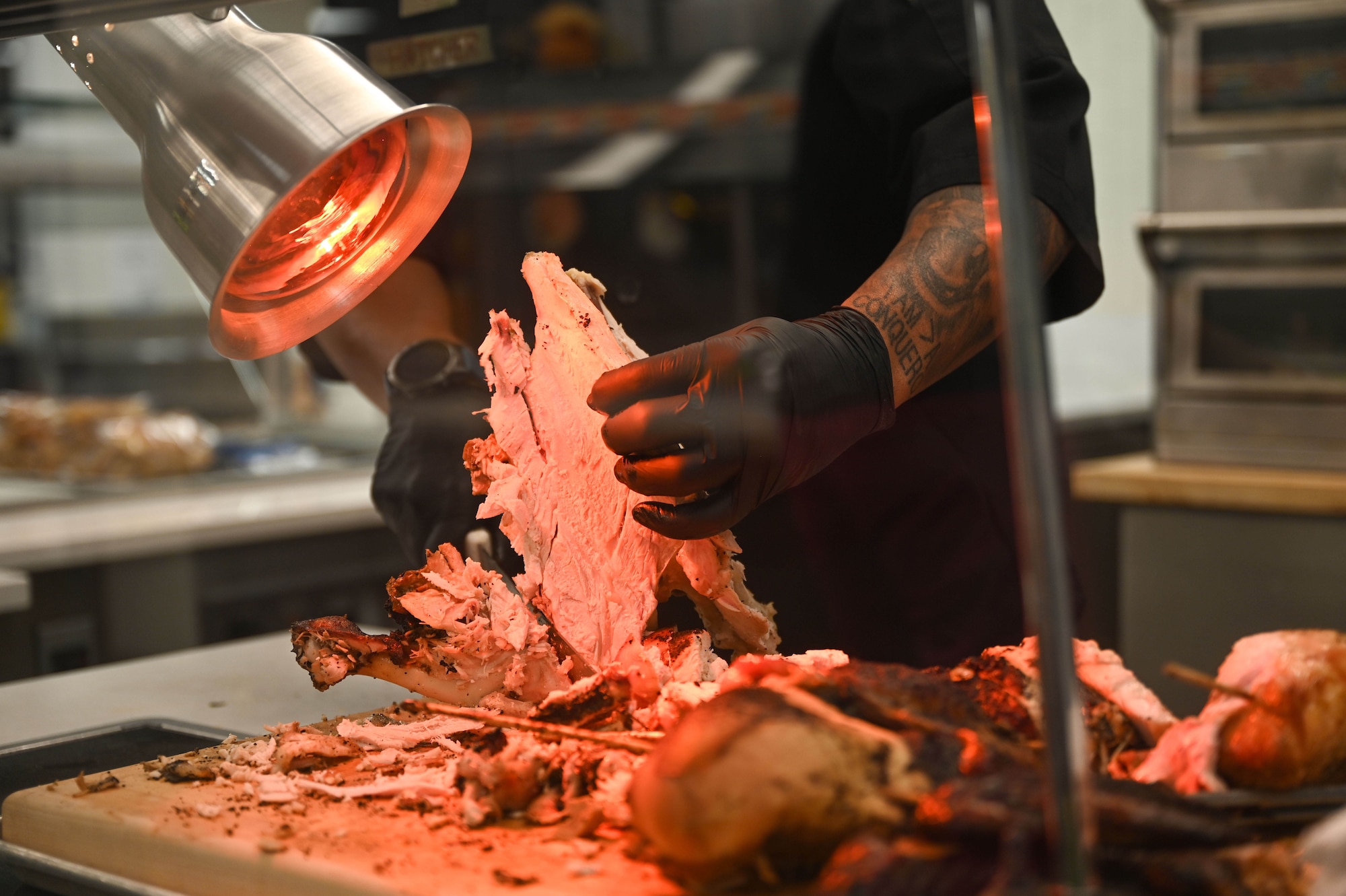 U.S. Air Force Chief Master Sgt. Kelvin Hatcher, 355th Wing Command Chief, carves a turkey to serve servicemembers, veterans and their families on Thanksgiving day at Davis-Monthan Air Force Base, Arizona, Nov. 27, 2025. The Desert Inn Dining Facility offered a full, traditional Thanksgiving meal with 355th Wing senior leaders continuing the longstanding military tradition of serving Airmen, Soldiers and other personnel the holiday meal. (U.S. Air Force photo by Staff Sgt. Kahdija Slaughter)
