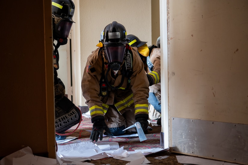 Firefighters crouch down at the entryway to a room.