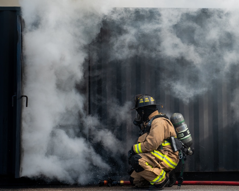 A firefighter kneels before a smokey building.