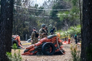 Airmen stand at defensive fighting positions fortified with orange and green sandbags and tires during a training course.