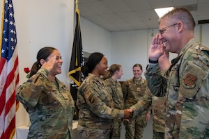 A line of female Airmen in military uniforms salute a Maj. Gen.