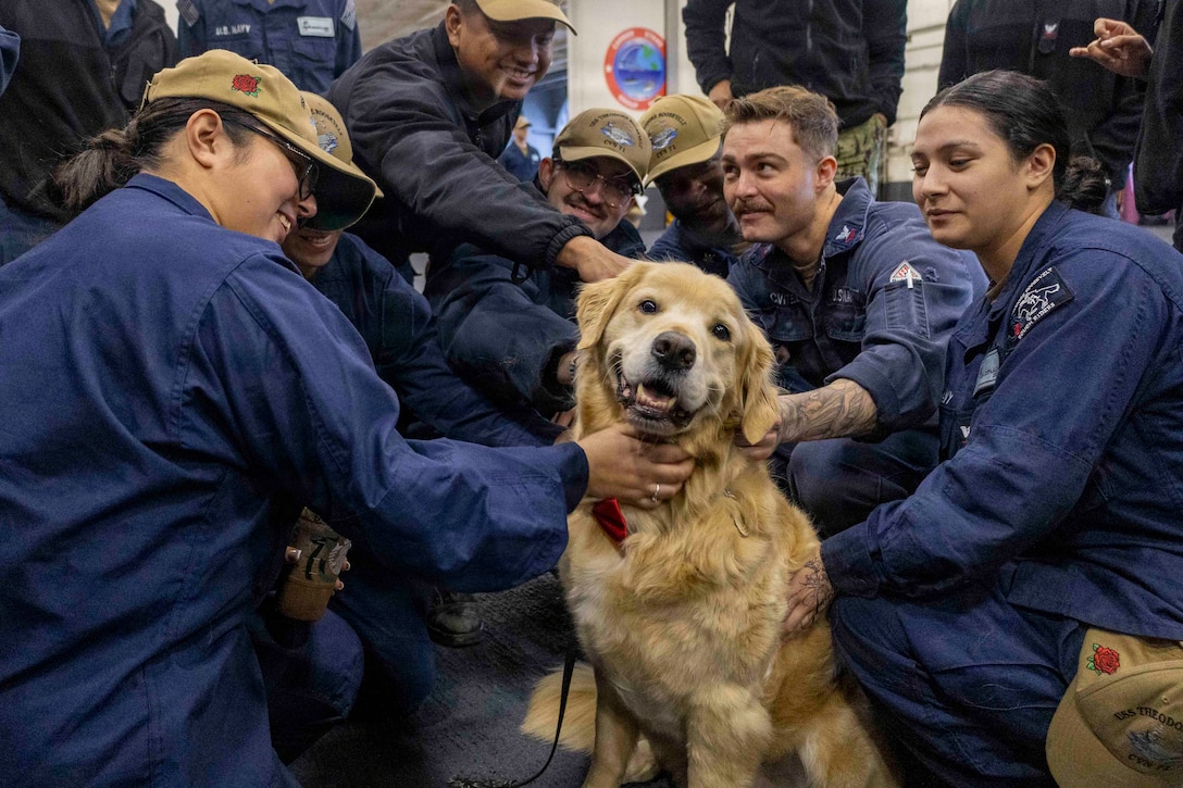 Sailors wearing blue jumpsuits pet a dog aboard a ship.