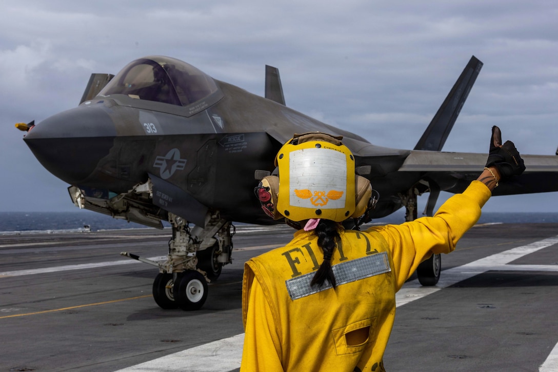 A sailor signals to an aircraft aboard a ship at sea.